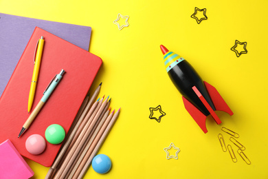 Photo of Bright toy rocket and school supplies on yellow background, flat lay