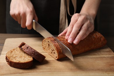 Photo of Woman cutting freshly baked rye baguette at wooden table, closeup