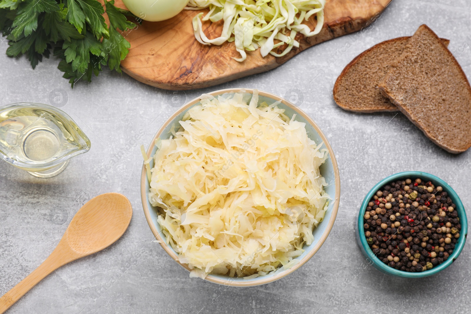 Photo of Bowl of tasty sauerkraut and ingredients on grey table, flat lay