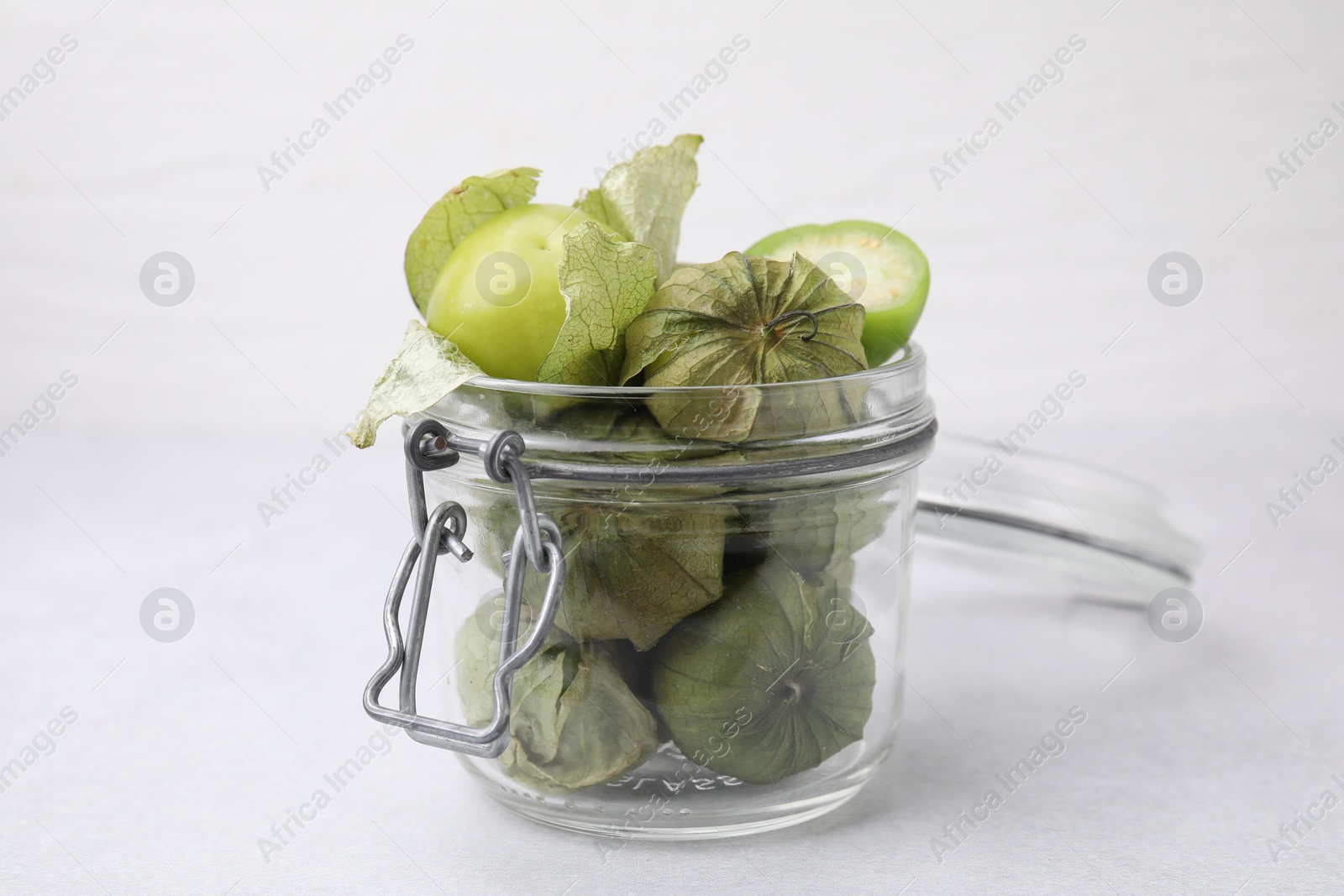 Photo of Fresh green tomatillos with husk in glass jar on table