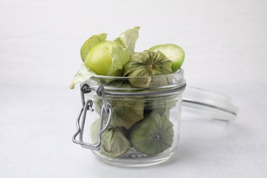 Fresh green tomatillos with husk in glass jar on table