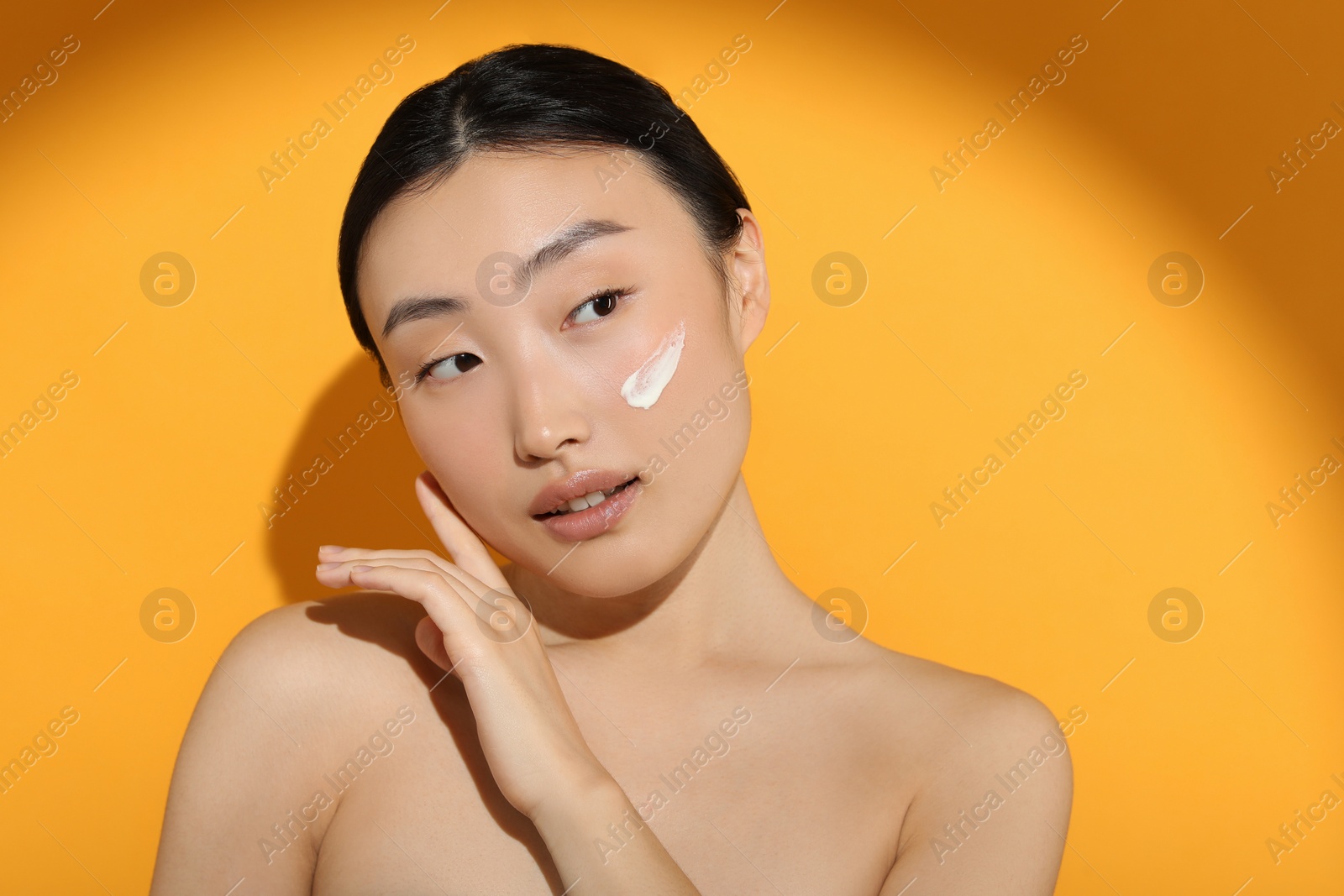 Photo of Beautiful young woman in sunlight with sun protection cream on her face against orange background, space for text