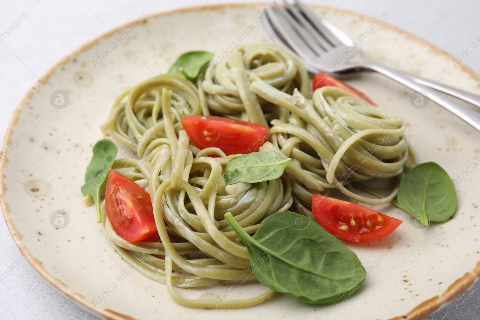 Photo of Tasty pasta with spinach, tomatoes and cutlery on light table, closeup