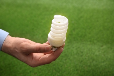 Photo of Man holding energy saving bulb for lamp against green grass, closeup