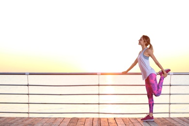 Photo of Young woman doing fitness exercises on pier in morning