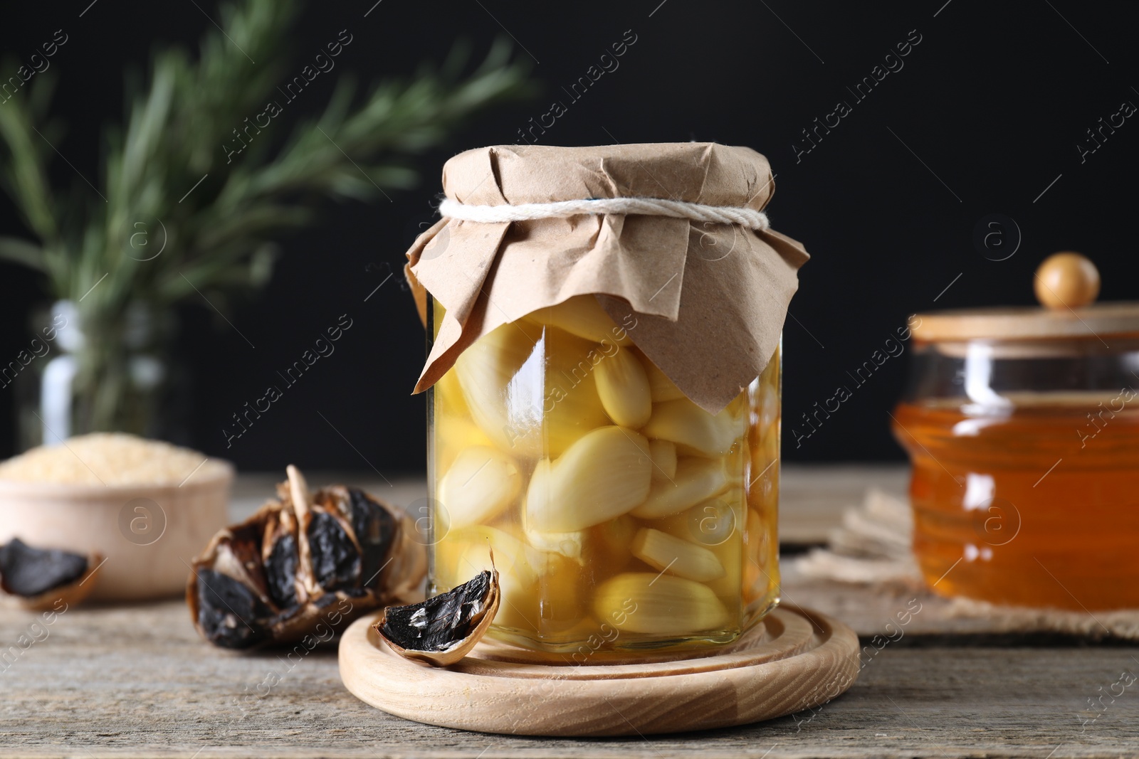 Photo of Garlic with honey in glass jar and fermented black garlic on wooden table