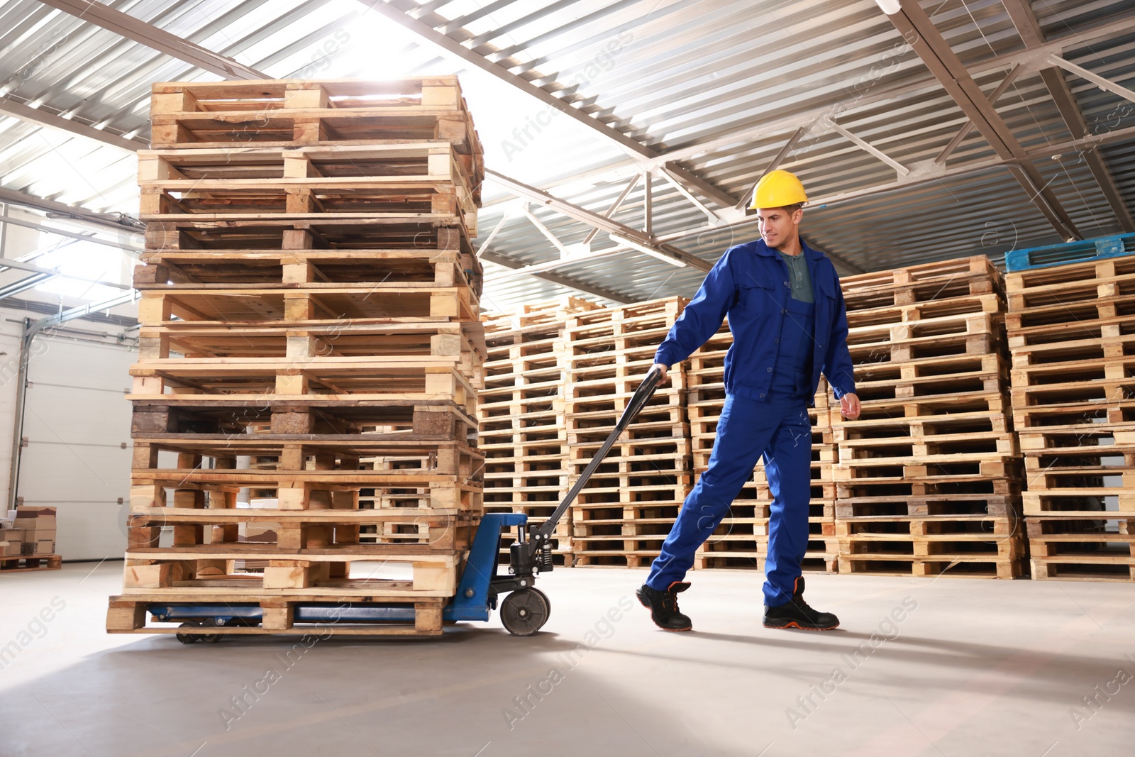 Image of Worker moving wooden pallets with manual forklift in warehouse