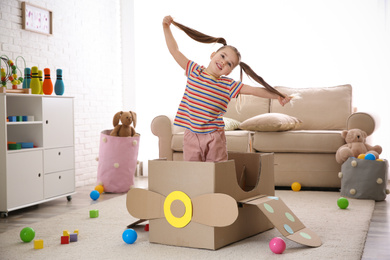 Photo of Cute little child playing with cardboard plane at home