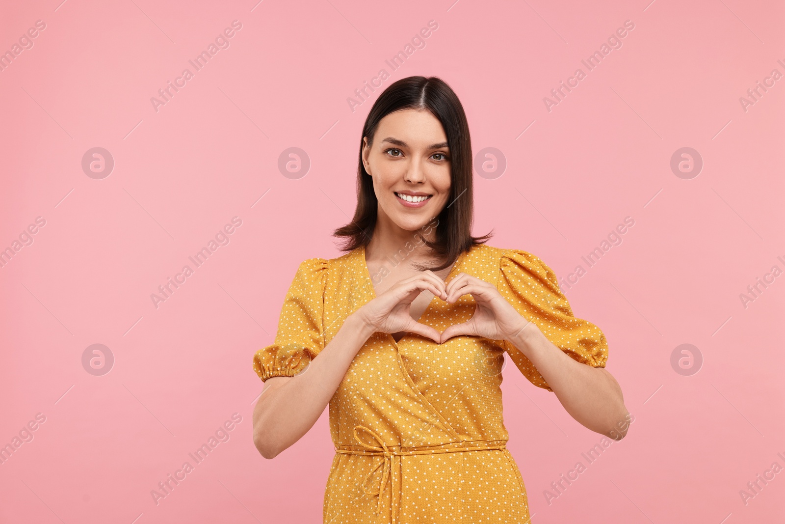 Photo of Young woman making heart with hands on pink background