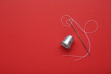 Silver thimble, needle and thread on red background, flat lay. Space for text