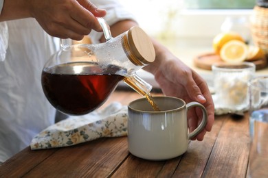 Photo of Woman pouring delicious tea into cup at wooden table, closeup
