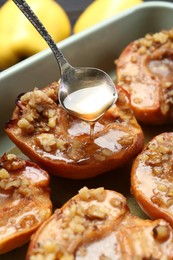 Photo of Pouring honey onto tasty baked quinces with nuts in dish, closeup