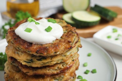 Photo of Delicious zucchini pancakes with sour cream served on table, closeup