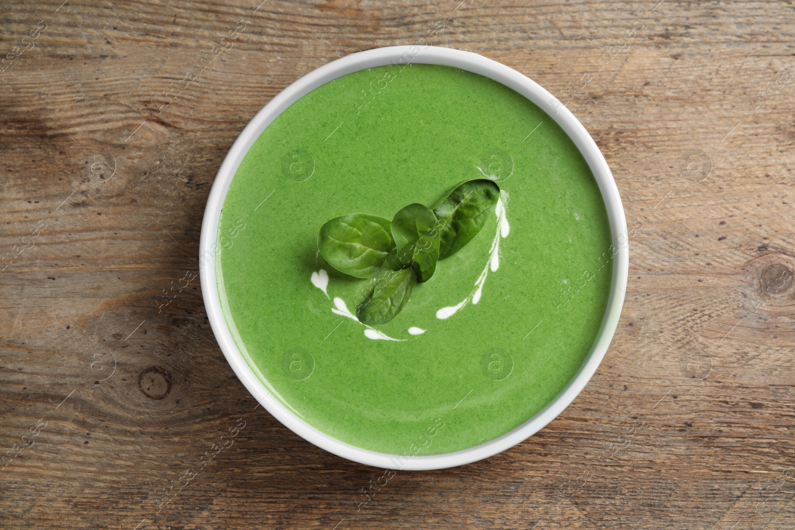 Photo of Bowl of healthy green soup with fresh spinach on wooden table, top view