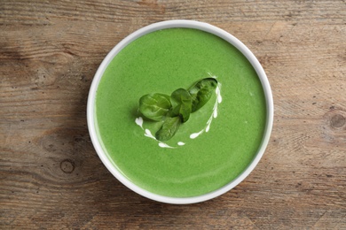 Photo of Bowl of healthy green soup with fresh spinach on wooden table, top view