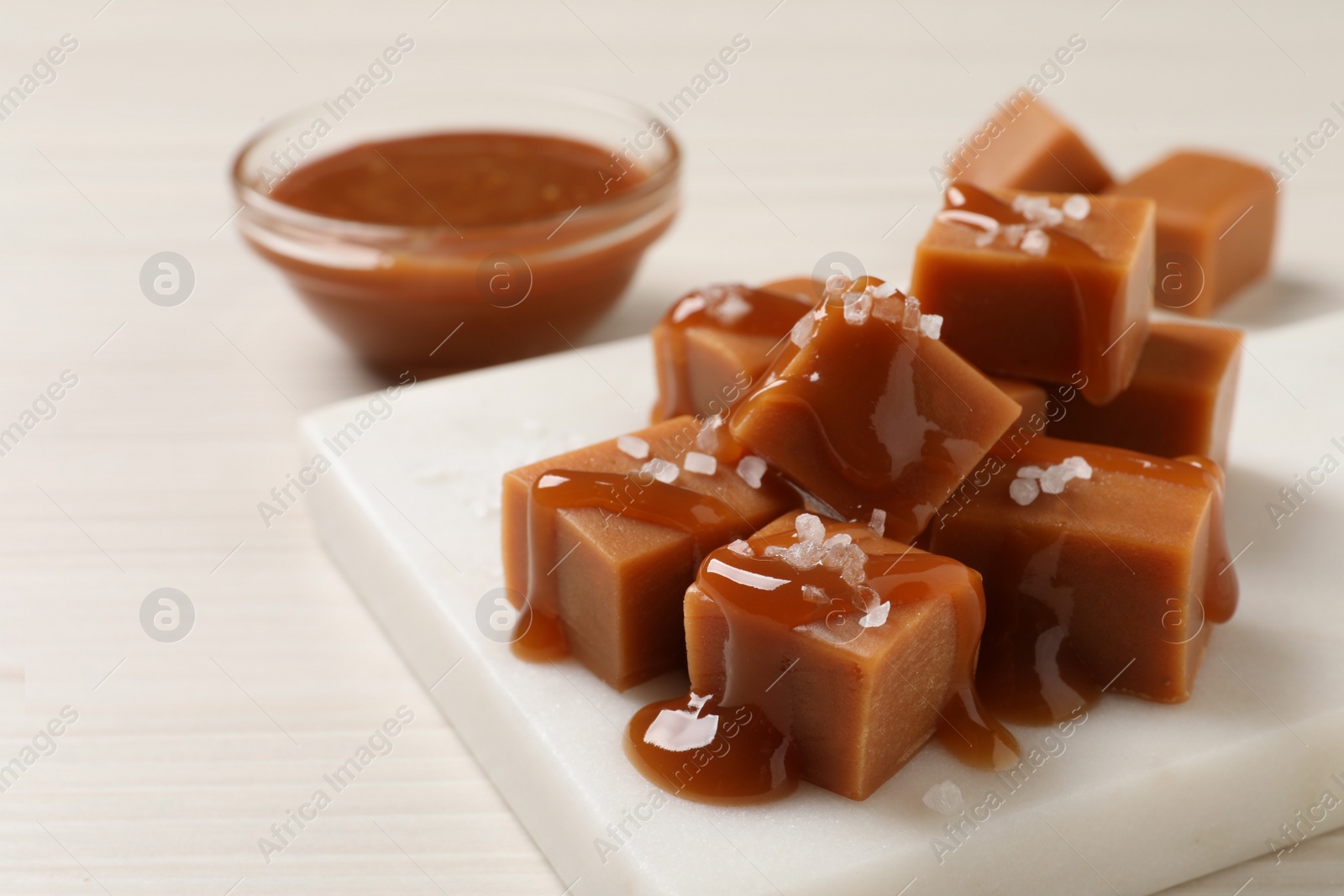 Photo of Tasty caramel candies with sauce and sea salt on white wooden table, closeup. Space for text