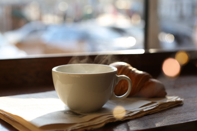 Photo of Delicious morning coffee, newspaper and croissant near window, indoors