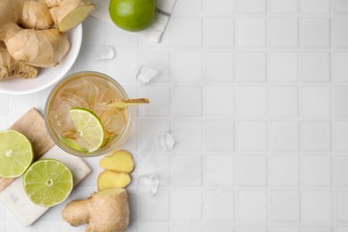 Photo of Glass of tasty ginger ale with ice cubes and ingredients on white tiled table, flat lay. Space for text