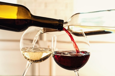Photo of Pouring delicious wine into glasses on light background