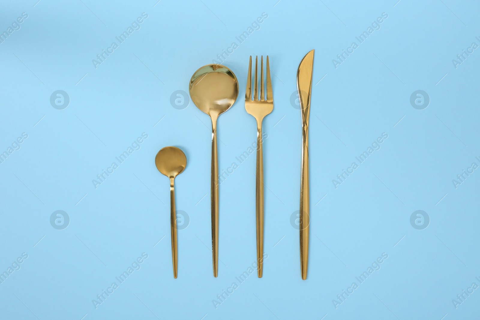 Photo of Stylish golden cutlery set on light blue background, flat lay