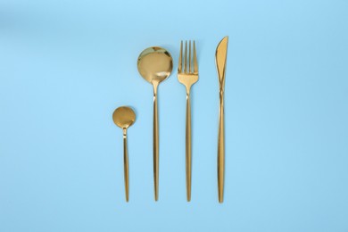 Photo of Stylish golden cutlery set on light blue background, flat lay
