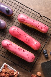 Tasty glazed eclairs, dry strawberries and blueberries on wooden table, flat lay