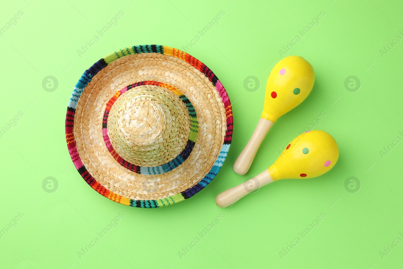 Photo of Mexican sombrero hat and maracas on green background, flat lay