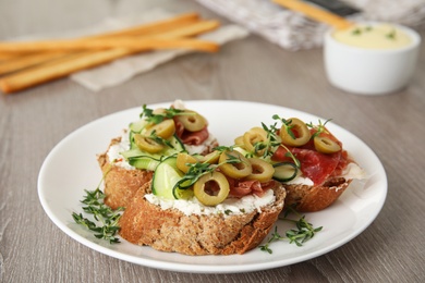 Photo of Plate of delicious bruschettas with prosciutto on grey wooden table