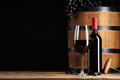 Photo of Delicious wine, wooden barrel and ripe grapes on table against black background. Space for text