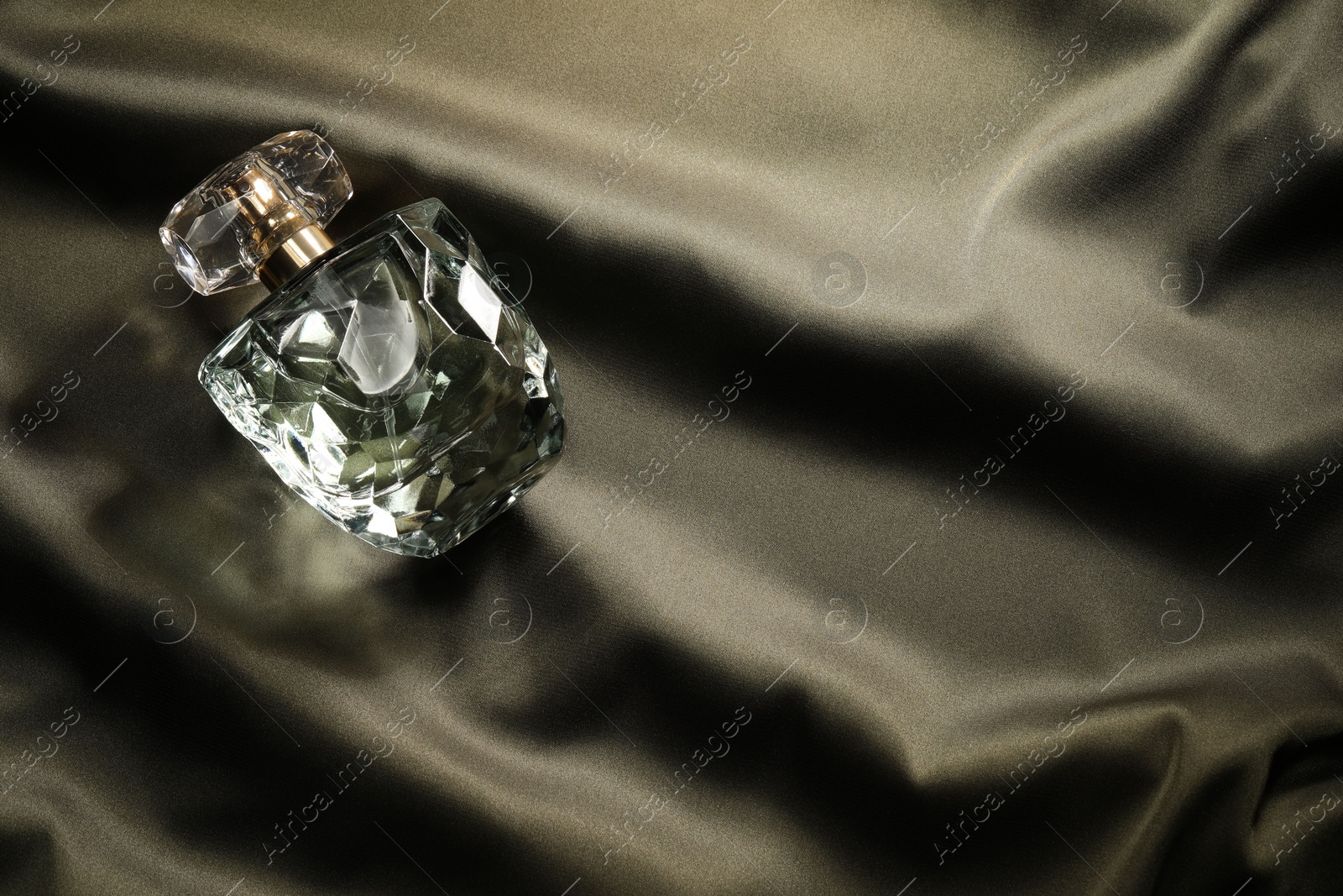 Photo of Luxury perfume in bottle on dark silk fabric, top view