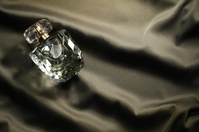 Luxury perfume in bottle on dark silk fabric, top view