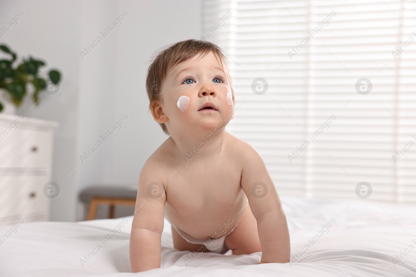Photo of Cute little baby with moisturizing cream on face on bed at home