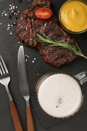 Mug with beer, delicious fried steak and sauce on black table, flat lay