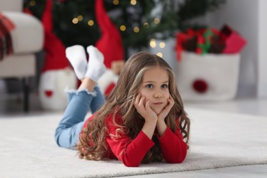Photo of Little girl lying on soft carpet at home. Christmas atmosphere