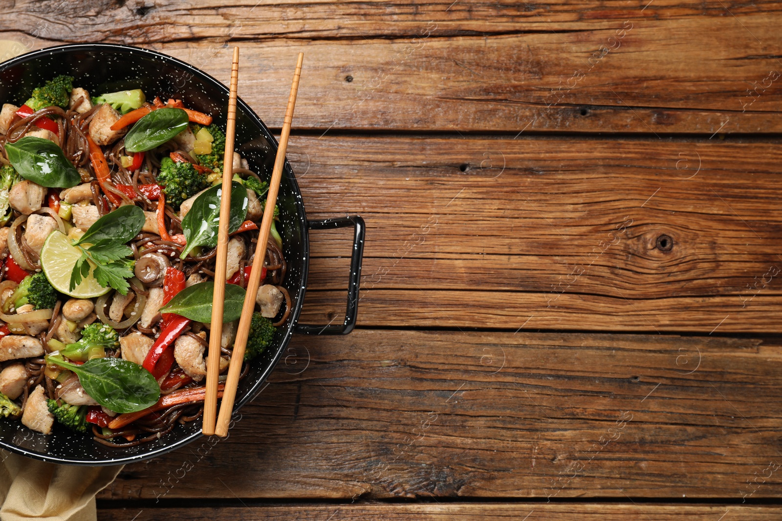 Photo of Stir-fry. Tasty noodles with meat in wok and chopsticks on wooden table, top view. Space for text