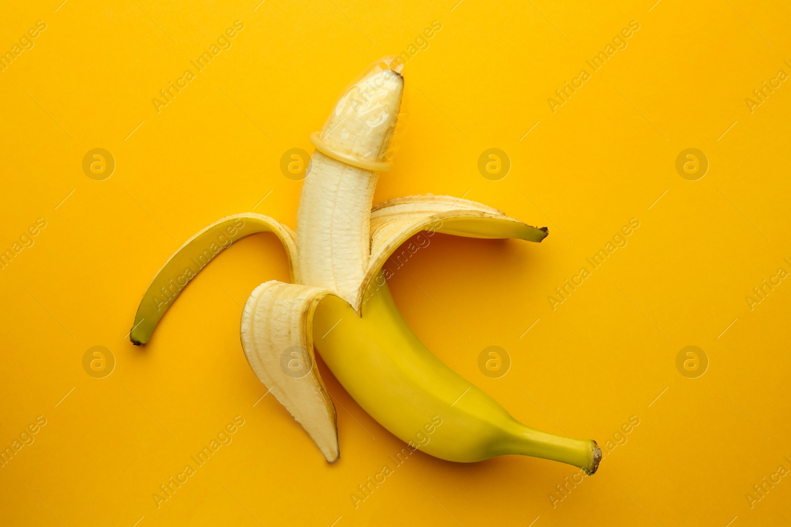 Photo of Banana with condom on orange background, top view. Safe sex concept