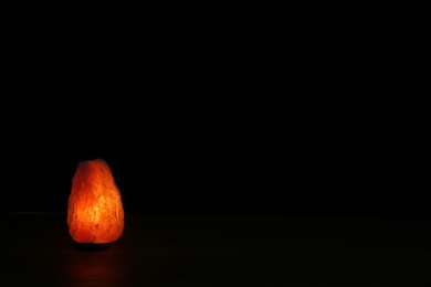 Photo of Himalayan salt lamp on black background. Space for text