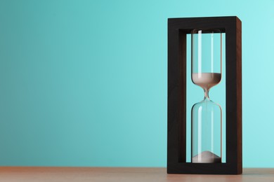 Hourglass with flowing sand on table against light blue background, space for text