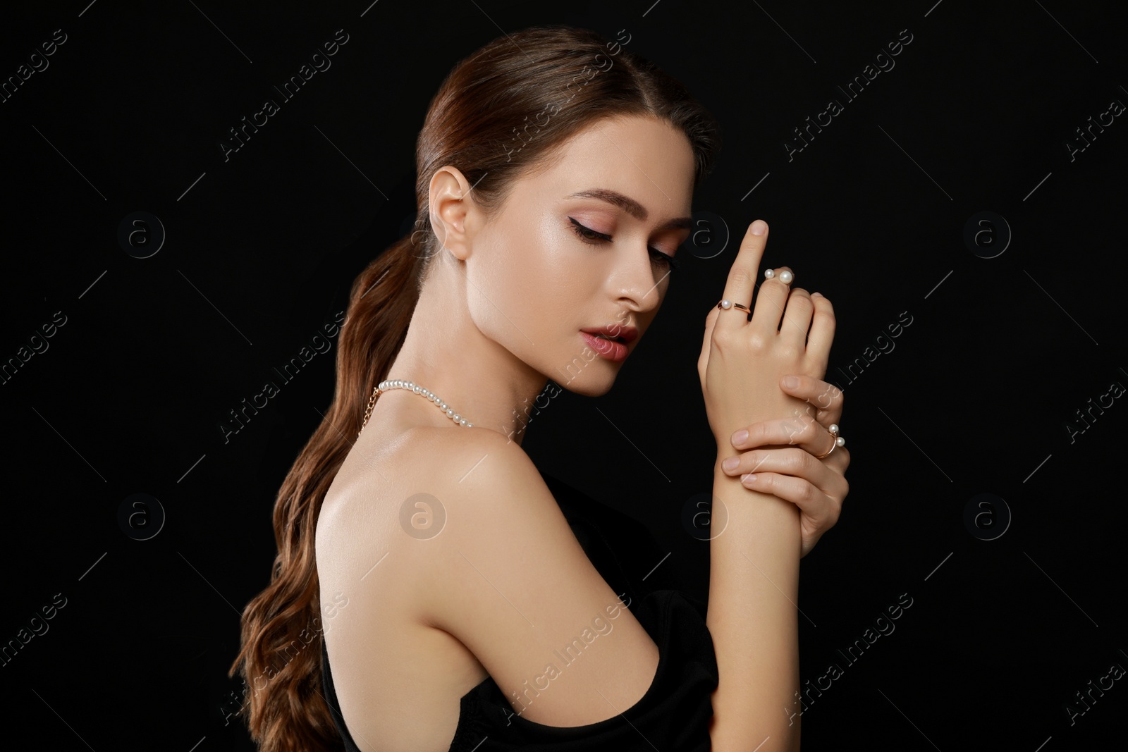 Photo of Young woman wearing elegant pearl jewelry on black background