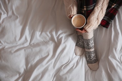 Woman with cup of coffee on soft blanket, top view. Space for text