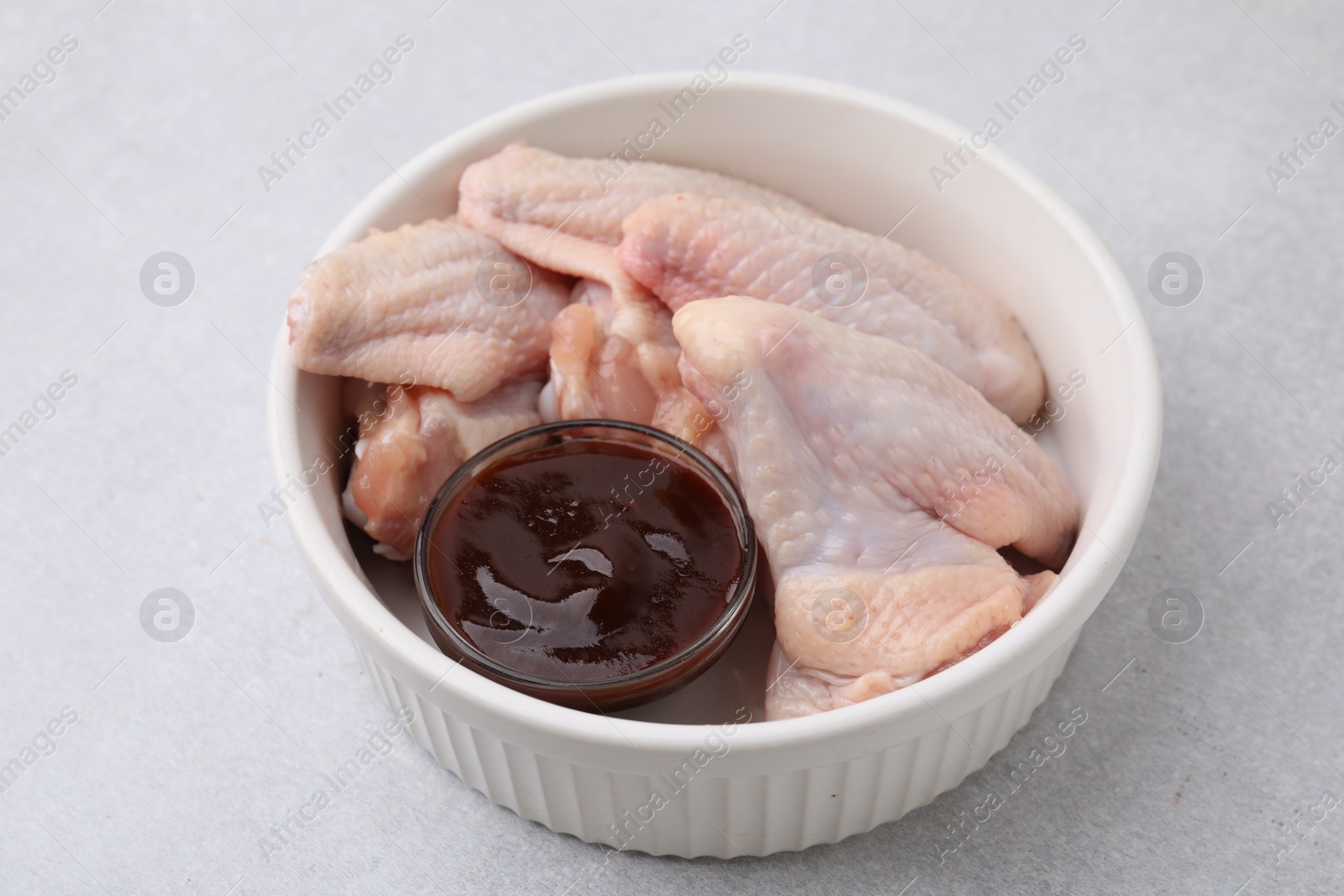 Photo of Plate with marinade and raw chicken wings on light textured table, closeup