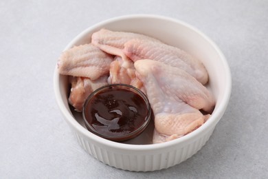 Plate with marinade and raw chicken wings on light textured table, closeup