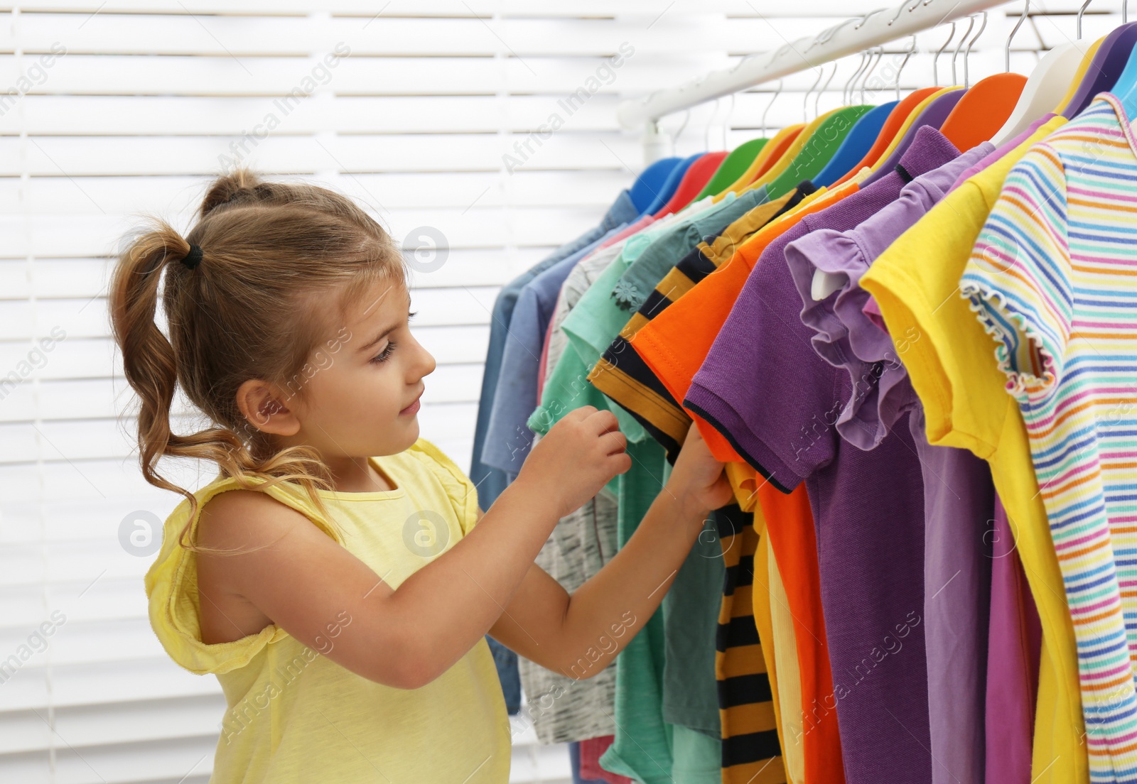 Photo of Little girl choosing clothes on rack indoors