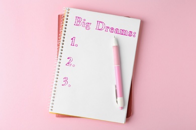 Image of Notebook with dreams list and pen on pink table, top view