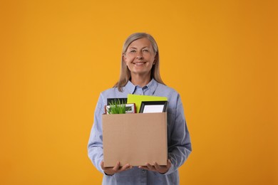 Photo of Happy unemployed senior woman with box of personal office belongings on orange background