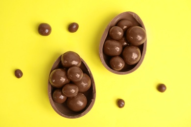 Halves of tasty chocolate egg with candies on yellow background, flat lay