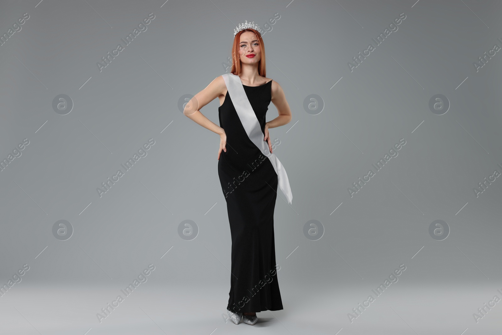 Photo of Beautiful young woman with tiara and ribbon in dress on light grey background. Beauty contest