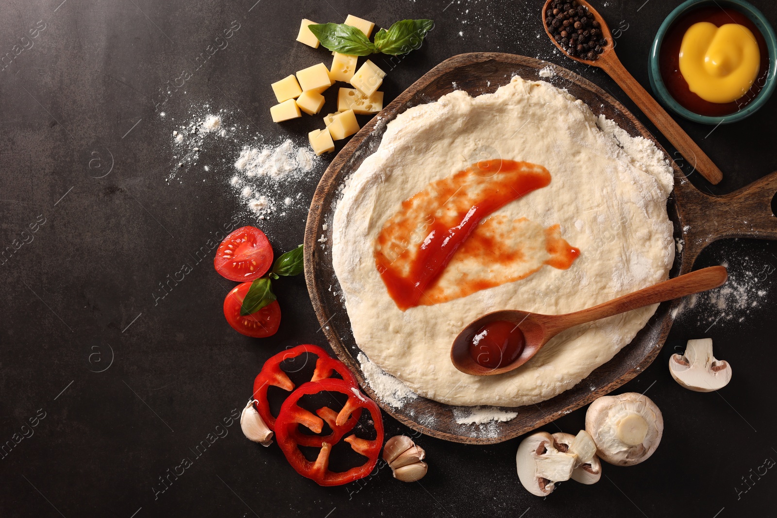 Photo of Pizza dough with tomato sauce and products on dark table, flat lay. Space for text