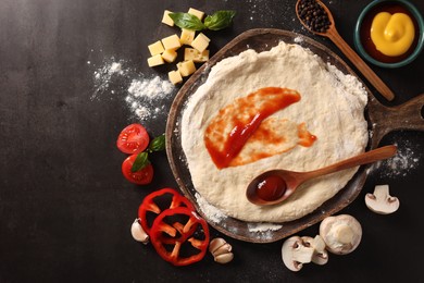 Photo of Pizza dough with tomato sauce and products on dark table, flat lay. Space for text