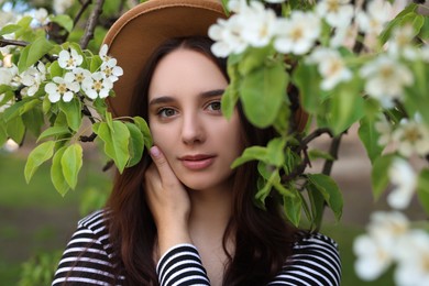 Beautiful woman in hat near blossoming tree on spring day